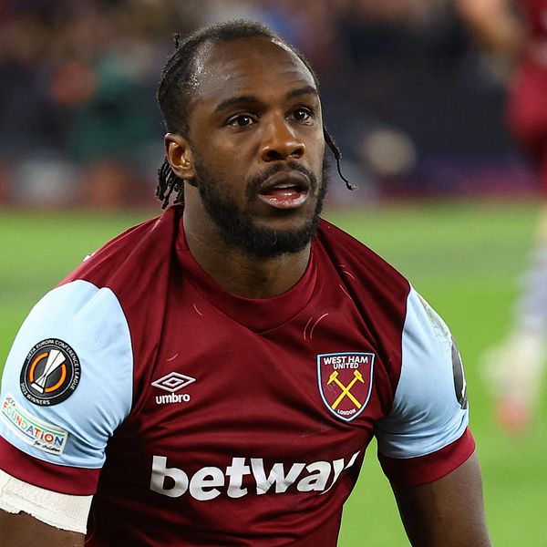 En spelare från West Ham United i en röd och ljusblå matchtröja, knäböjer på planen efter en intensiv situation under en match. I bakgrunden syns andra spelare och åskådare på stadion.