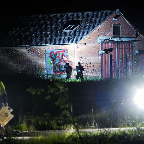 Polis undersöker området vid en nedgången lada nattetid, stark belysning i förgrunden.