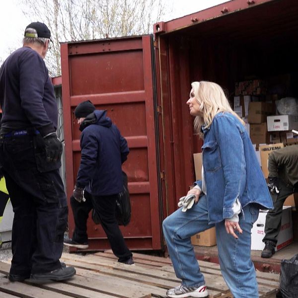 flera personer står vid en container och en kvinna tittar in i ett lastbilsflak.