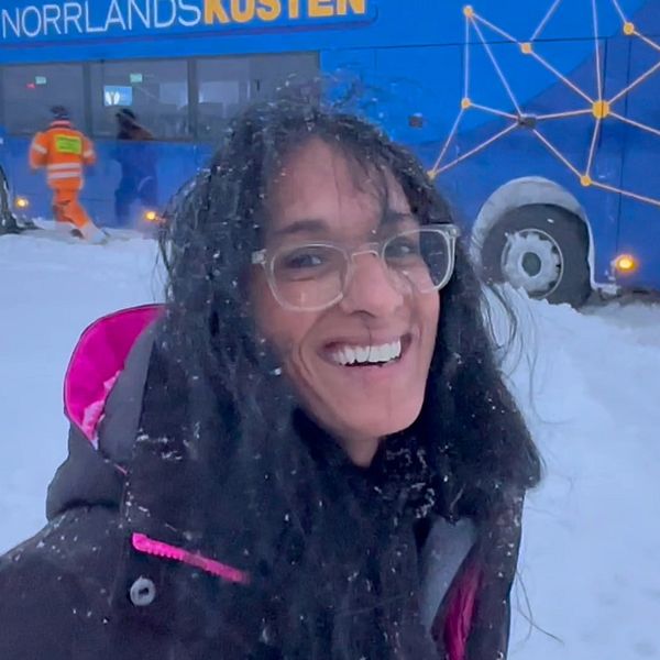 En skrattande kvinna i snöfall framför en buss som fastnat.
