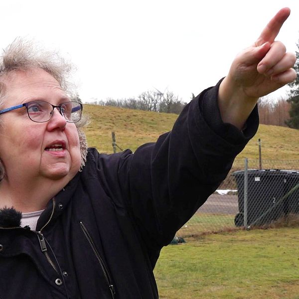 Kvinna i sin trädgård som pekar ut ett vindkraftverk några hundra meter från tomtgränsen.