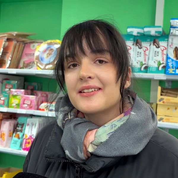 Person i en butik, omgiven av diverse matvaror på hyllor.