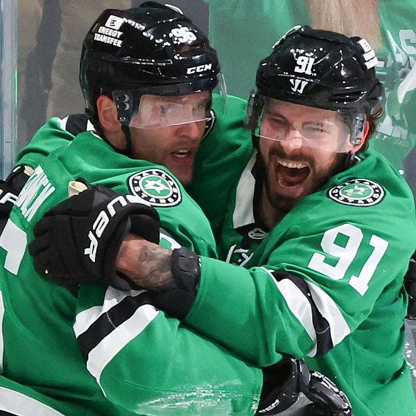 Två ishockeyspelare i gröna Dallas Stars-tröjor firar med en kram på isen.