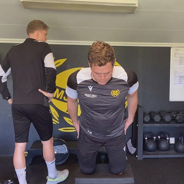 Tre fotbollsspelare tränar i ett gym med kettlebells och en anslagstavla i bakgrunden.
