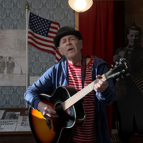 Owe ”Clapson” Carlsson spelar gitarr i ett rum som dekorerats med amerikanska flaggor, gamla fotografier och stående silhuetter av musiker med dragspel.