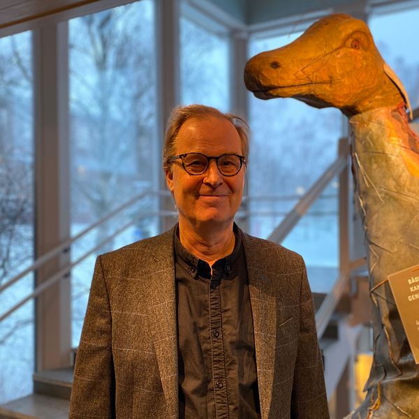 Museiechefen Olov Amelin står framför en skulptur av Storsjöodjuret på Jamtli. Utanför fönstret syns snöiga träd i bakgrunden.
