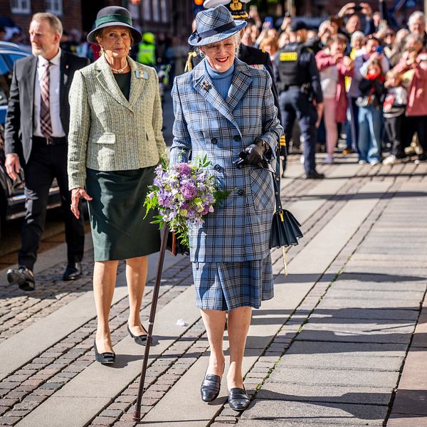 Drottning Margrethe går med blombukett framför publik på en solig gata.
