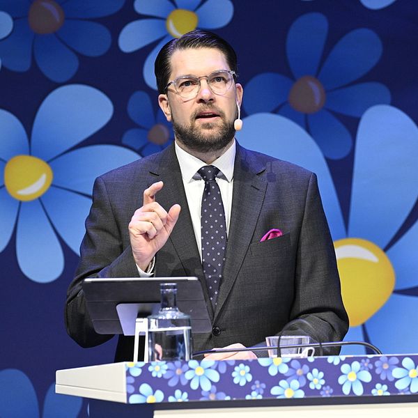 Åkesson framför en fondvägg täckt av blommor.