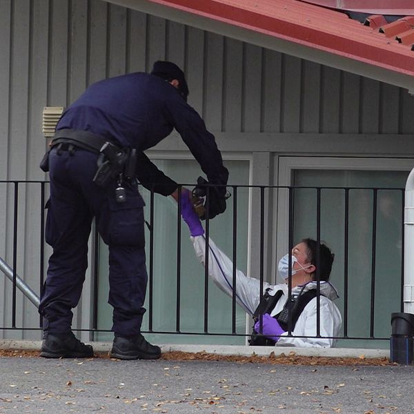 En polis och en tekniker står i en trapp och räcker något till varandra