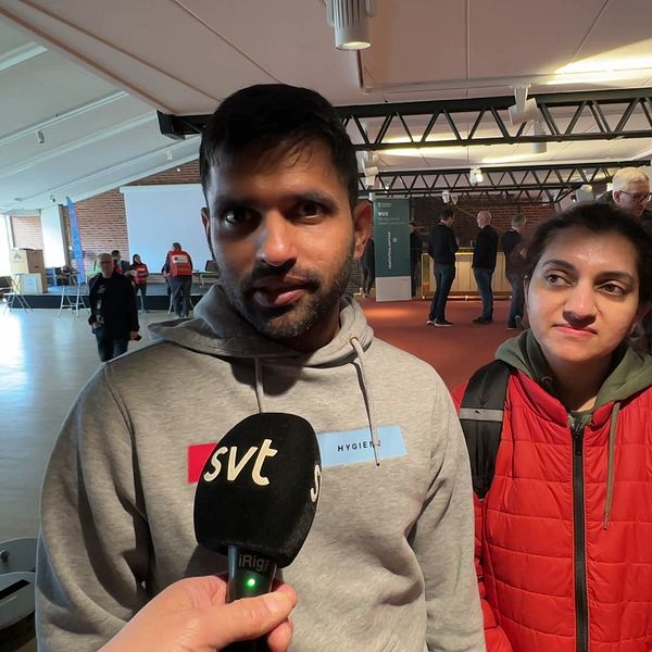 En man och en kvinna intervjuas av SVT i en inomhusmiljö med människor i bakgrunden