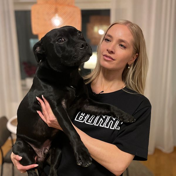Kvinna håller i en svart hund i sitt hem.