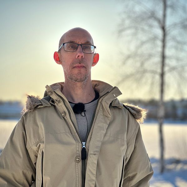 Man i täckjacka står i motljus vid Lillfjärden, Hudiksvall.