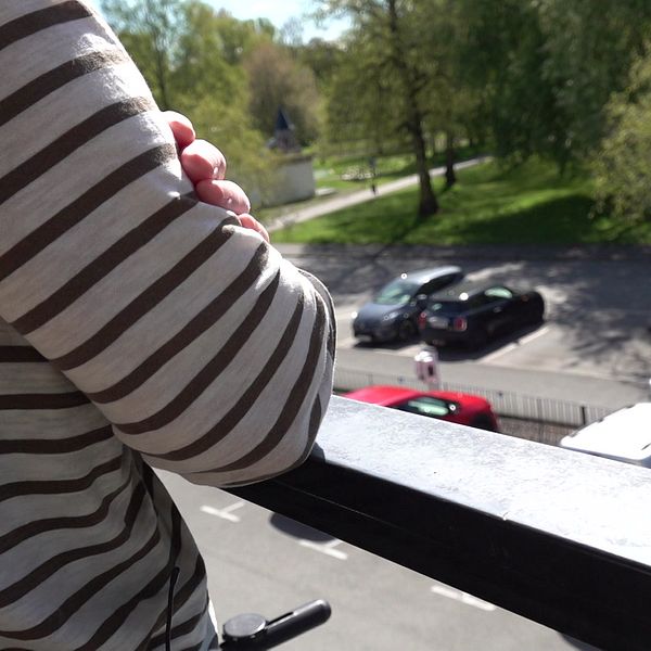 Person i randig tröja lutar sig mot balkongräcke och tittar ner mot parkering och grönområde.