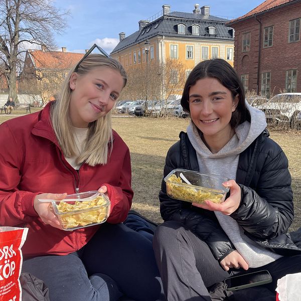 Två personer sitter på gräs och äter intill Stockholms nation.