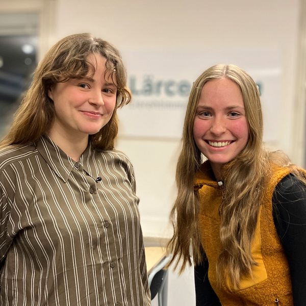 Emma Gunnarsson till vänster med brunt smålockigt hår och Maja Modig med långt hår och en fleeceväst, står i ett klassrum på campus Åre.