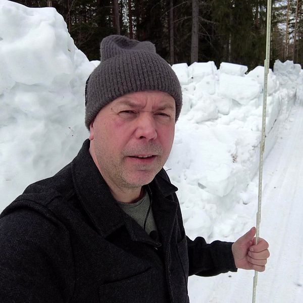 Reporter Patrik Samuelsson med en tumstock vid höga snövallar