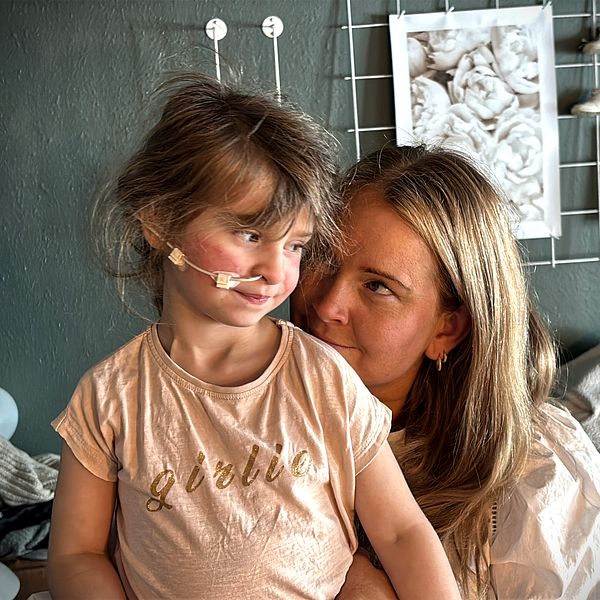 Evelina Bygg håller sin dotter Tyra i famnen i ett vardagsrum.