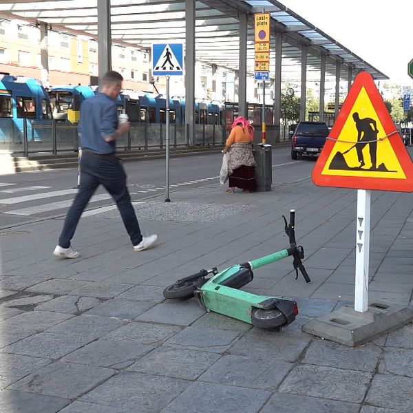 En elsparkcykel ligger felparkerad på trottoaren i Stockholm nära ett vägarbetsmärke.