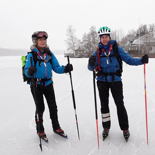 Två kvinnor som står på isen med långfärdsskridskor och utrustning