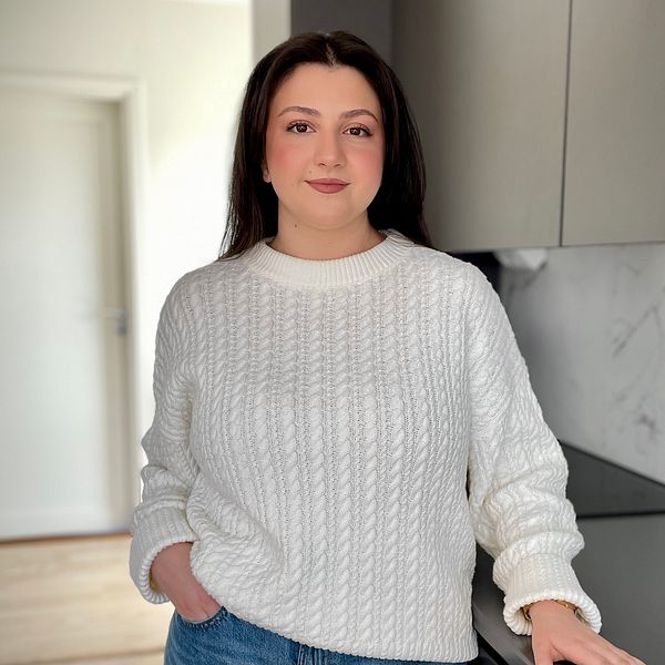 Person i vit stickad tröja står i ett modernt kök med gråa skåp och marmormönstrad vägg.