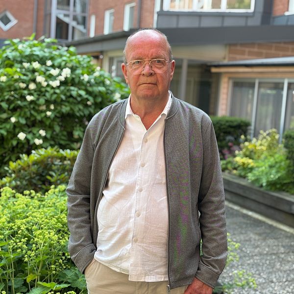 En person står i en grönskande innergård framför bostadshus.