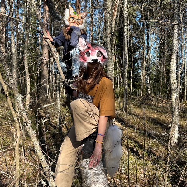 Två personer i djurmasker klättrar i träd i en skog.