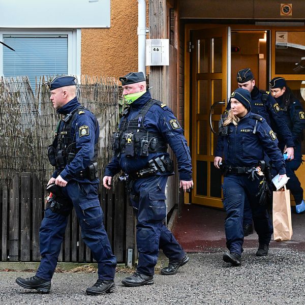 Poliser lämnar en byggnad, en bär en papperspåse.