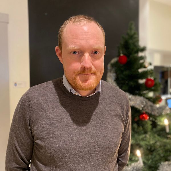 Östersunds kommunstyrelseordförande, Niklas Daoson (S) står framför en julgran dekorerad med röda kulor och silverfärgad girlang, inomhus i en festlig miljö.