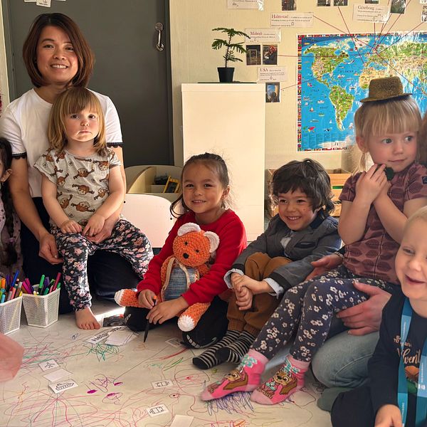 En grupp barn sitter på golvet med leksaker, leksakskarta och pedagog.