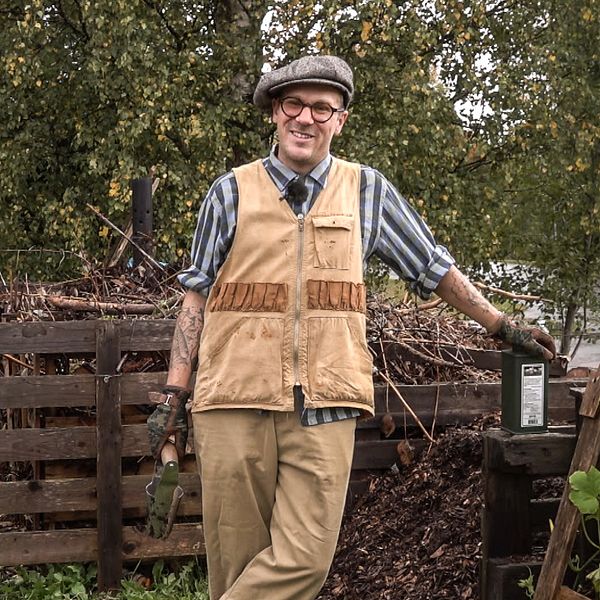 Trädgårdsmästaren Markus Rosendal står vid sin höstträdgård med olika växter och blommor i bakgrunden. Personen har på sig en rutiga skjorta och en väst.