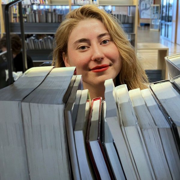 Kvinna med ljust hår bakom böcker i bibliotek, Olivia Rosén vid Karlstads universitet, vinnare av Lilla Psykologipriset 2024