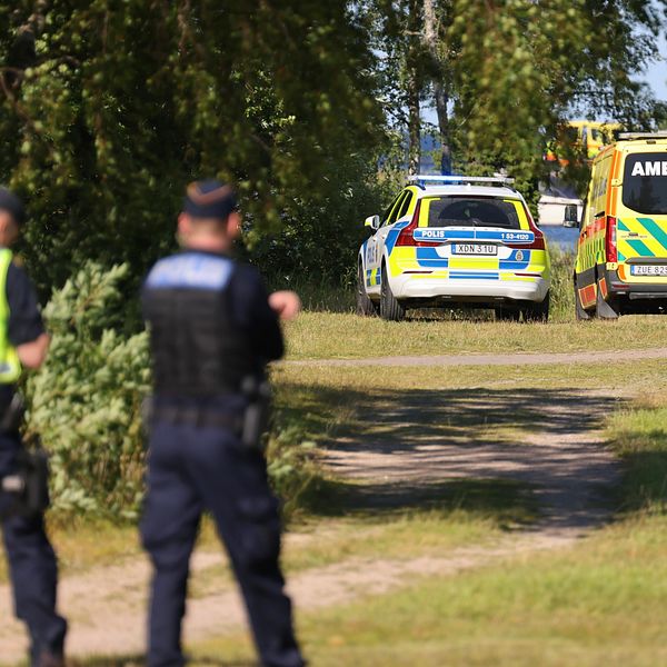 Poliser tittar mot vatten där en polisbil och en ambulans står.
