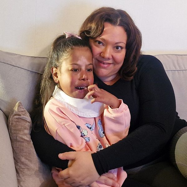 Olivia Jawad sitter i en soffa och håller om dottern Janiyah i sitt knä.