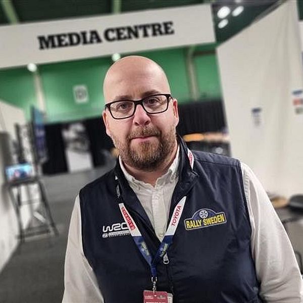 Eric Åström står i en mediecenterlokal med entréskyltar och kontorsmöbler i bakgrunden.