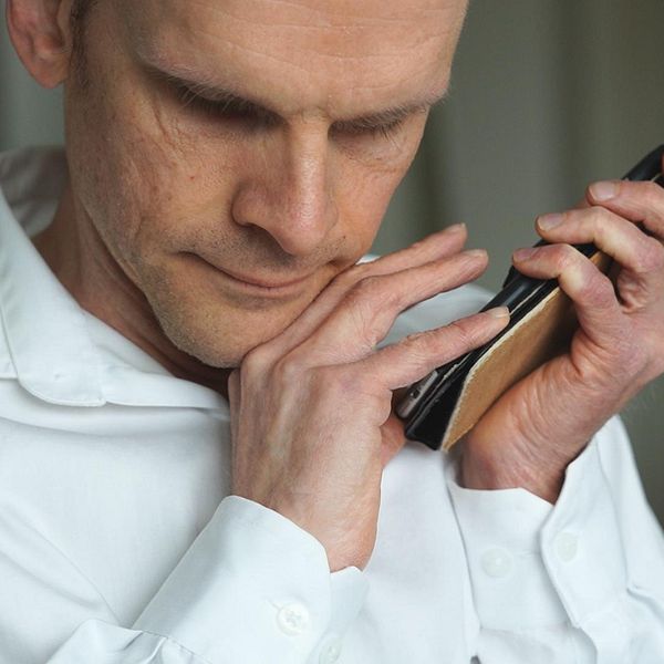 Närbild på Henrik Götesson, i vit skjorta, som håller upp sin telefon med båda händerna, mot ena örat. Ansiktet är vänt lite nedåt mot telefonen.