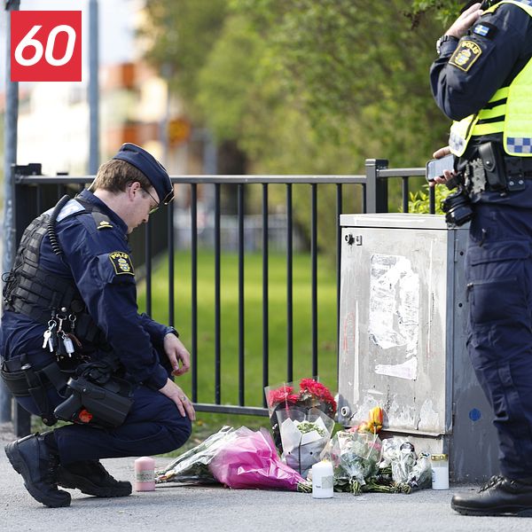 Två poliser vid ett blomhav på trottoaren, minnesplats efter händelse utomhus.