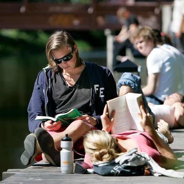 Två kvinnor läser böcker på en brygga i solen.