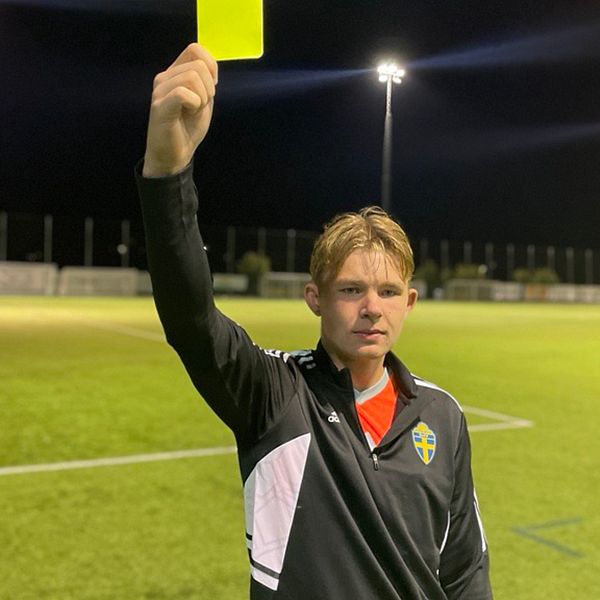 En ung kille som är fotbollsdomare och håller upp i ett gult kort