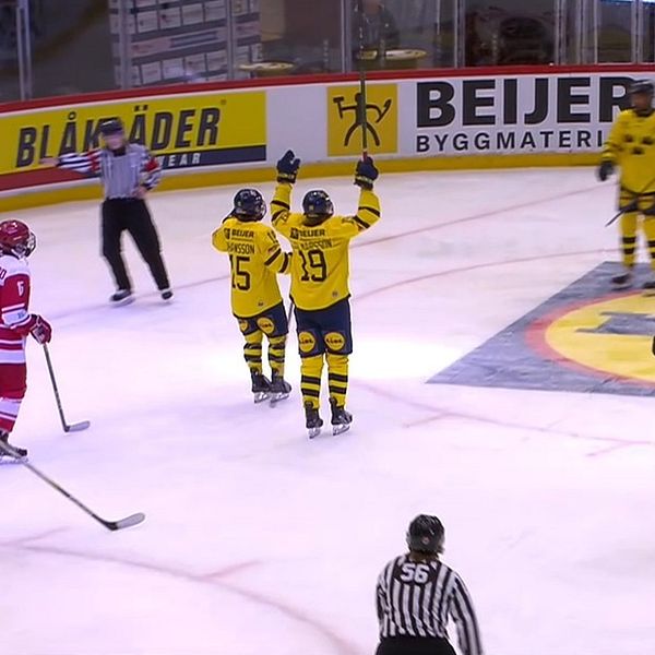 Spelare i gula tröjor jublar efter att ha gjort mål i en ishockeymatch medan spelare i röda tröjor reagerar vid målet och på isen. Domare vakar över spelet på isen.