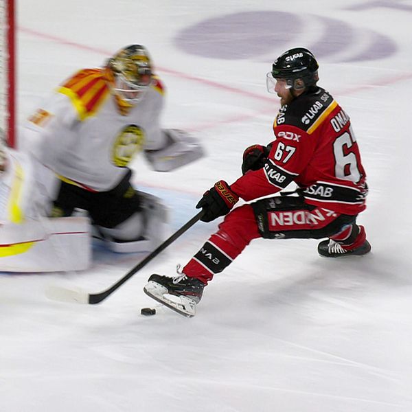 Hockeyspelare i röd tröja utmanar målvakt i vit dräkt under match framför målbur.