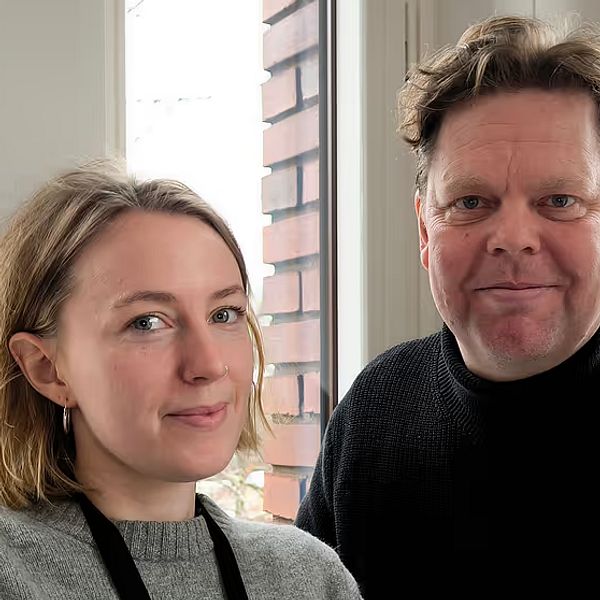 Håkan Wikström och Moa Roos står bredvid varandra inomhus vid ett fönster.