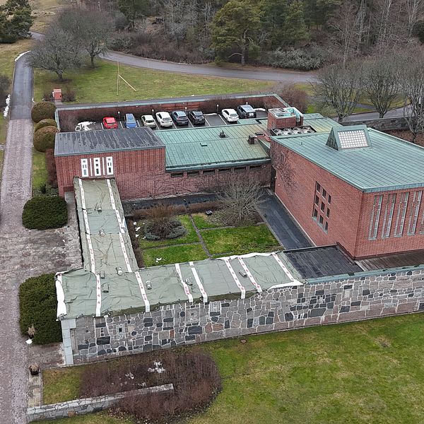 Flygbild över en tegelbyggnad med parkeringsplats omgiven av grönska.