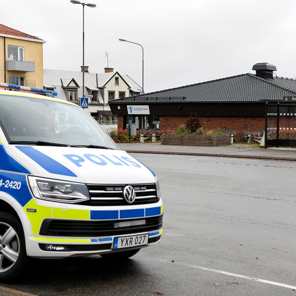En polisbil parkerad vid en busshållplats på en gatan i mellerud med socialkontoret i bakgrunden och en mulen himmel.
