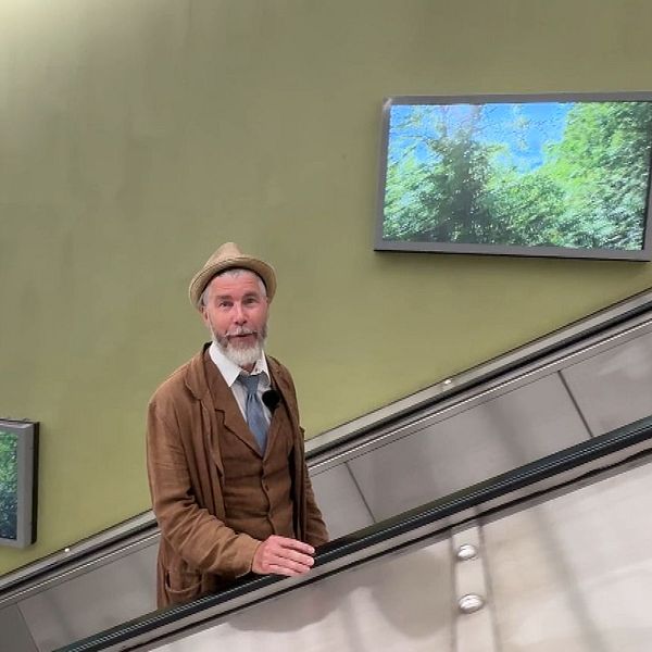 Jan Rydén Bonmot åker rulltrappa i tunnelbana med naturbilder på väggen.