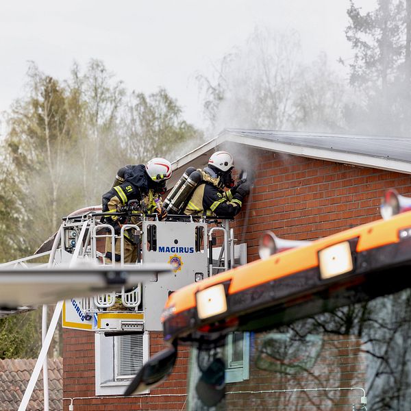 två brandmän arbetar med att släcka en brand på taket tillhörande en villa.