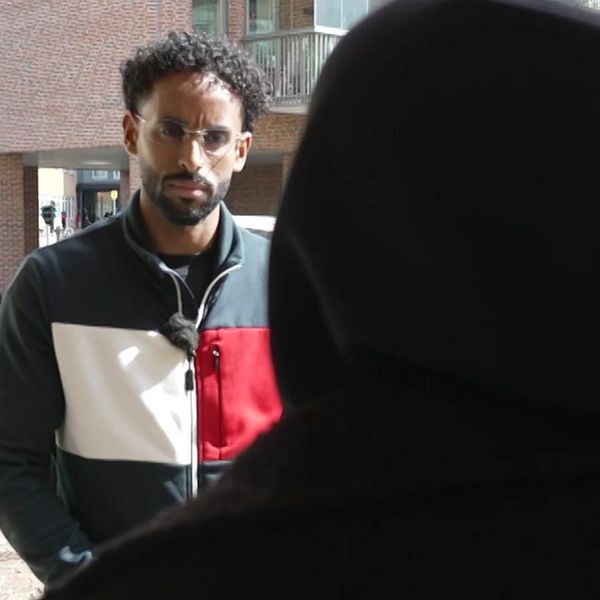 Två personer samtalar utomhus vid en husentré i ett bostadsområde.