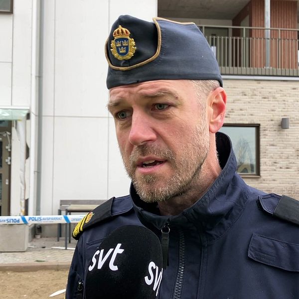 Anders Persson, Falkenbergspolisens operativa samordnare, i polisuniform står framför en byggnad med en trasig dörr och fönster, omgivet av avspärrningar.