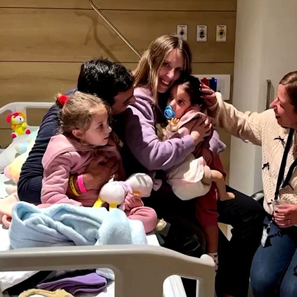 Familj sitter på sjukhussäng, föräldrar kramar om sina döttrar.
