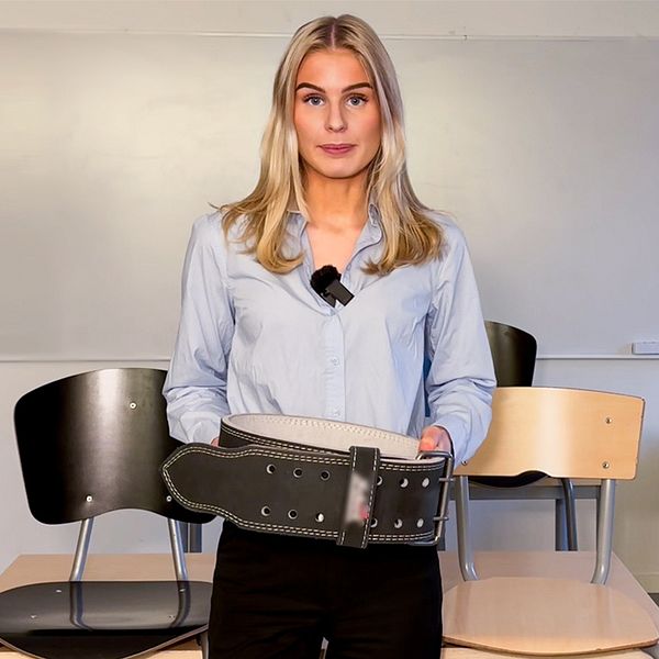 Alva Olsson, reporter på SVT, står i ett klassrum och håller i ett tyngdlyftarbälte.