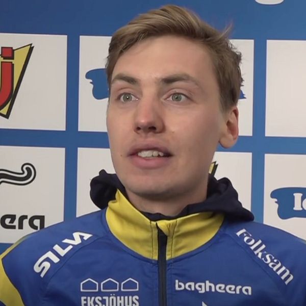 Person i blågul sportjacka framför sponsorvägg med logotyper.